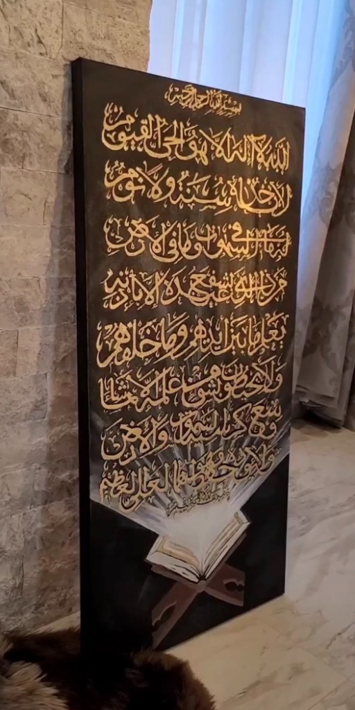 Large Ayatul Kursi painting on dark canvas with gold calligraphy and Quran stand
